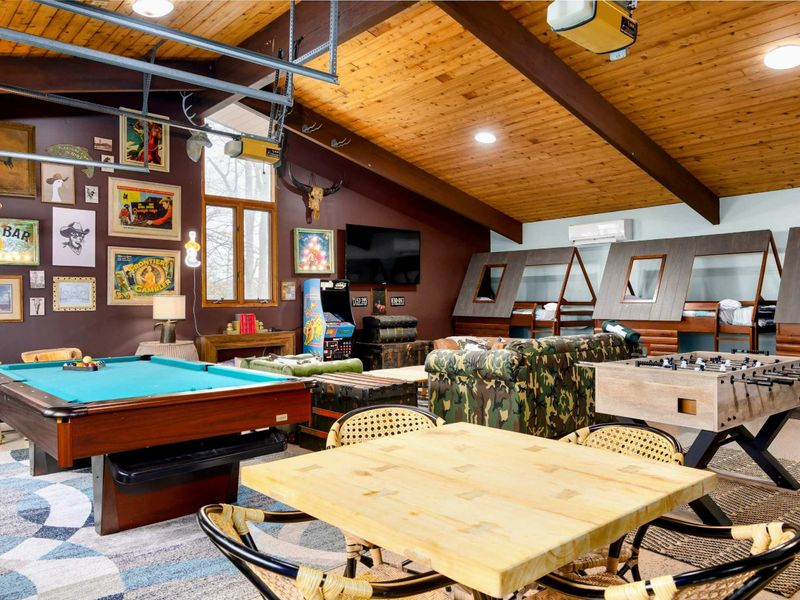 The Game Room is packed with entertainment, featuring a pool table, foosball, arcade games, cozy seating, and custom-built bunk beds, all surrounded by rustic decor for endless fun and relaxation.