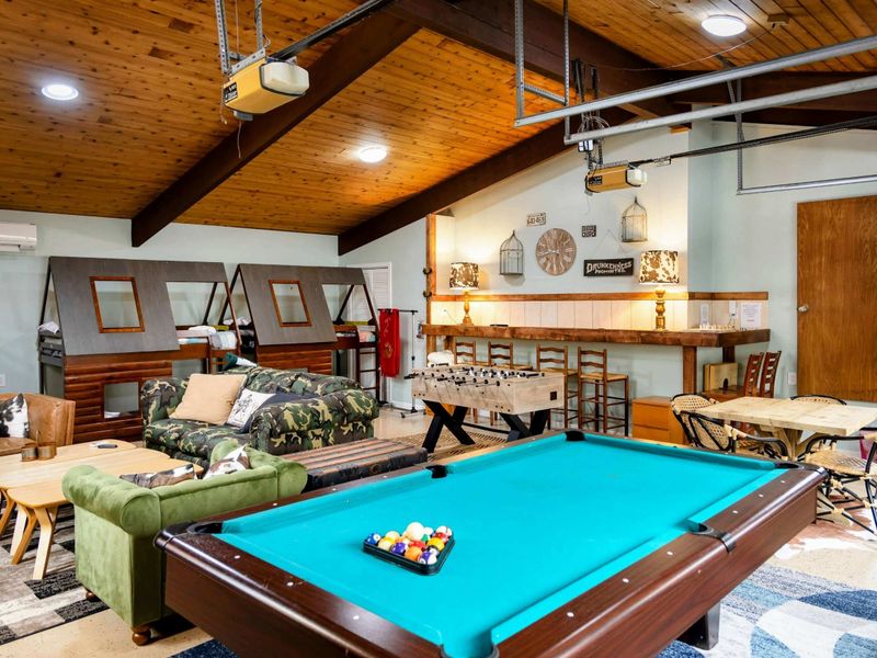 The Game Room offers a spacious retreat with pool and foosball tables, cozy lounge seating, unique bunk-style beds, and a rustic bar area for ultimate relaxation and entertainment.