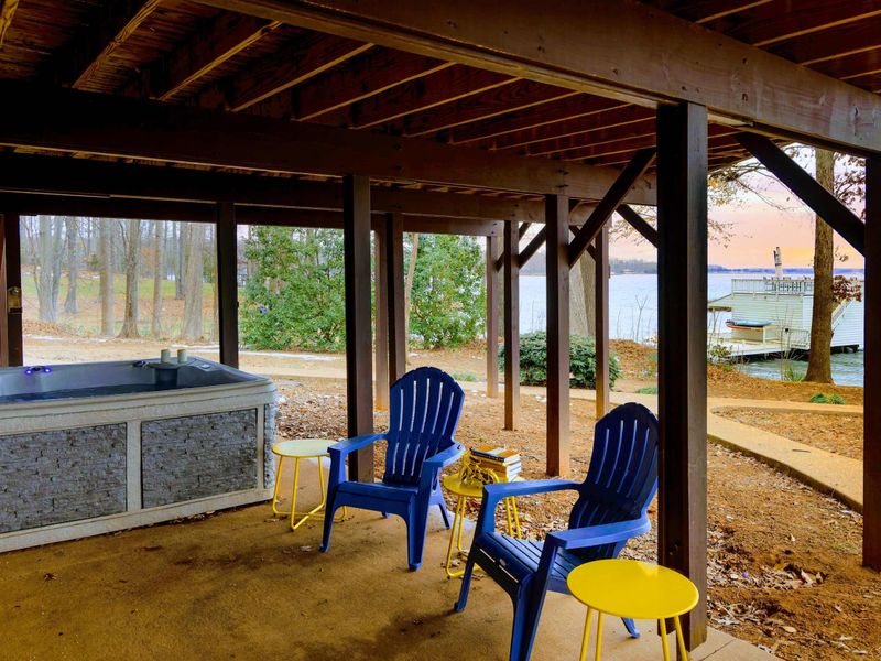 This inviting space, located under the deck, features a private hot tub and cozy seating with vibrant accents, offering serene lake views and a perfect spot to relax after a day on the water.