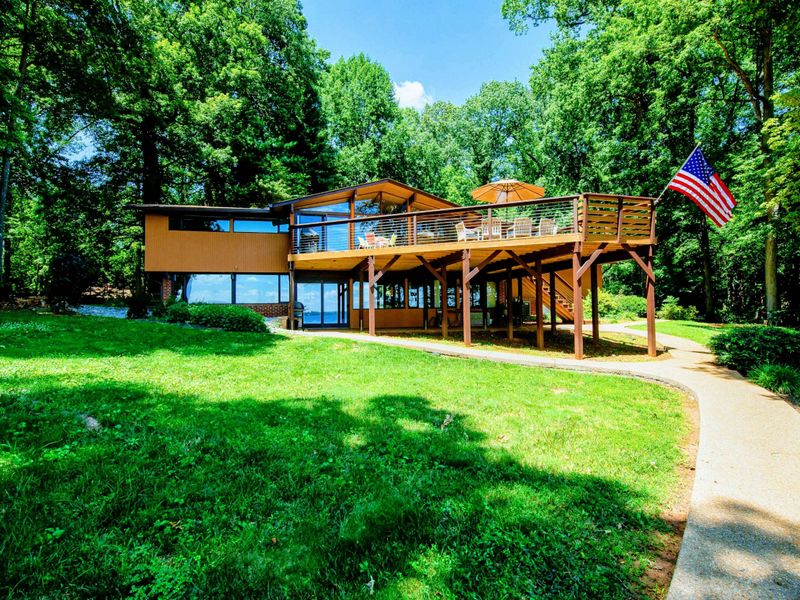 Spacious lakefront home with a large elevated deck, modern architecture, and serene wooded surroundings.