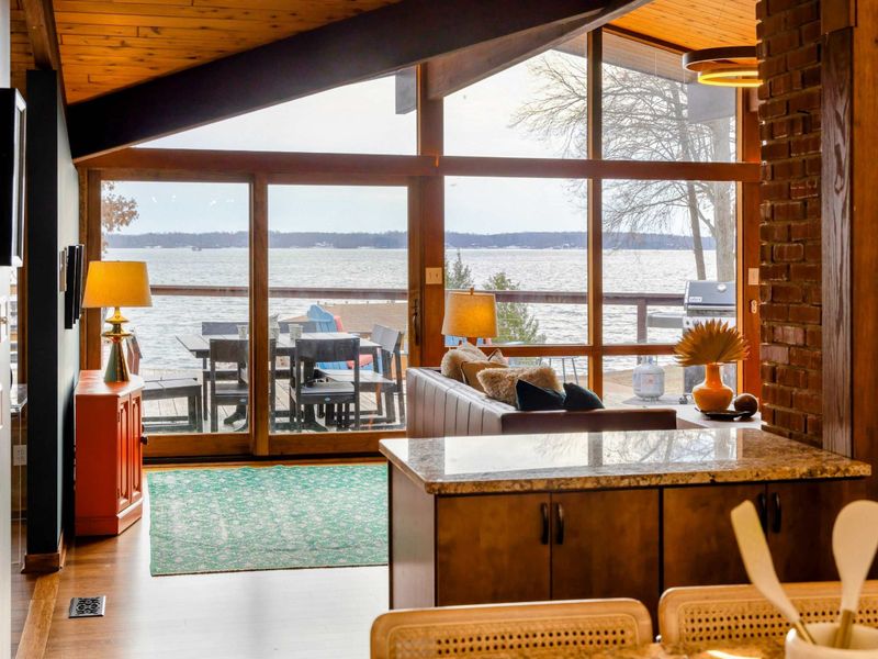 The Great Room seamlessly connects indoor elegance with outdoor charm, offering breathtaking views of the lake through expansive windows that lead directly to the spacious deck, perfect for dining or lounging by the water.