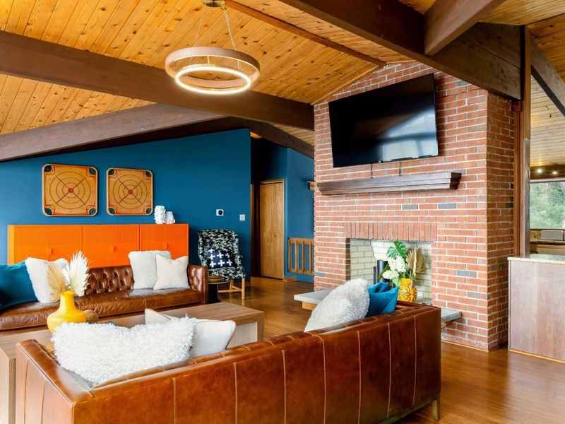 The Great Room features a warm and inviting design with a vaulted wooden ceiling, plush leather seating, and a central brick fireplace topped with a flat-screen TV, creating the perfect space for relaxation and entertainment.