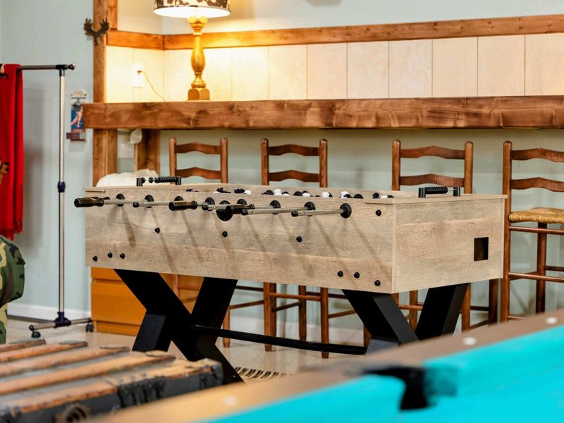The Game Room includes a sleek foosball table positioned near a rustic bar setup, adding to the room's charm and offering a perfect spot for fun and casual entertainment.