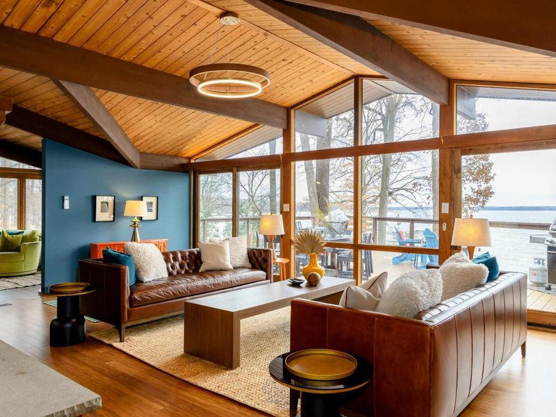 The Great Room showcases elegant leather seating, warm wooden accents, and floor-to-ceiling windows that frame breathtaking lake views, creating a perfect blend of comfort and natural beauty.