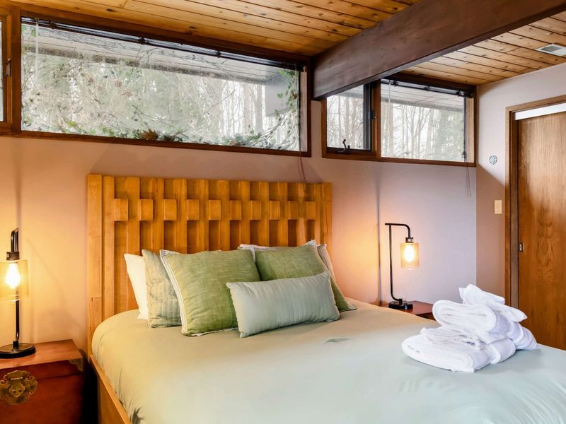 This bedroom offers a tranquil atmosphere, featuring a distinctive woven wooden bed frame and warm ambient lighting. A stack of fresh towels adds a welcoming touch.