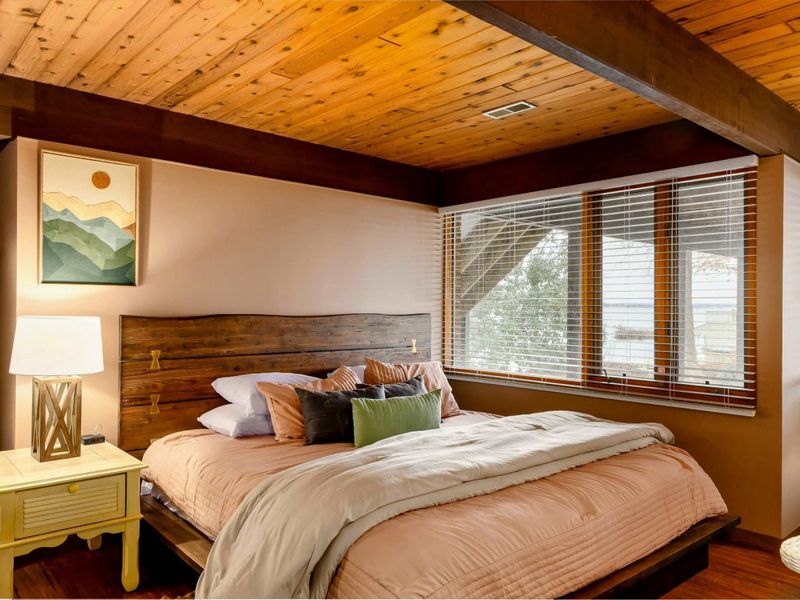 This cozy bedroom showcases a rustic wood bed frame complemented by large windows that invite in natural light and offer tranquil views of the outdoors.