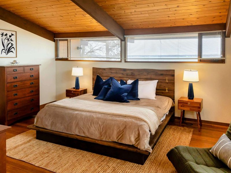 A serene primary suite featuring a rustic wooden bed frame, cozy bedding, and stylish side tables with modern lamps, creating a relaxing retreat.