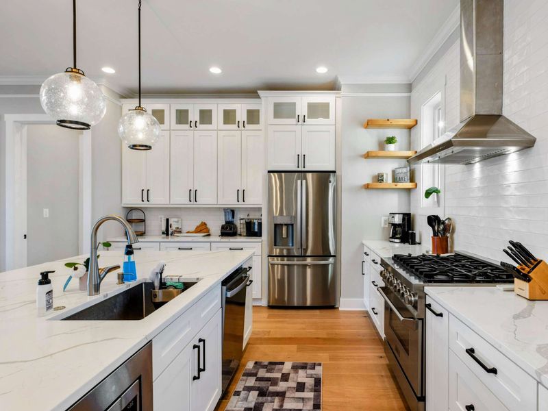 A modern and fully equipped kitchen with stainless steel appliances, elegant white cabinetry, a large center island, and stylish lighting for a perfect cooking and dining experience.