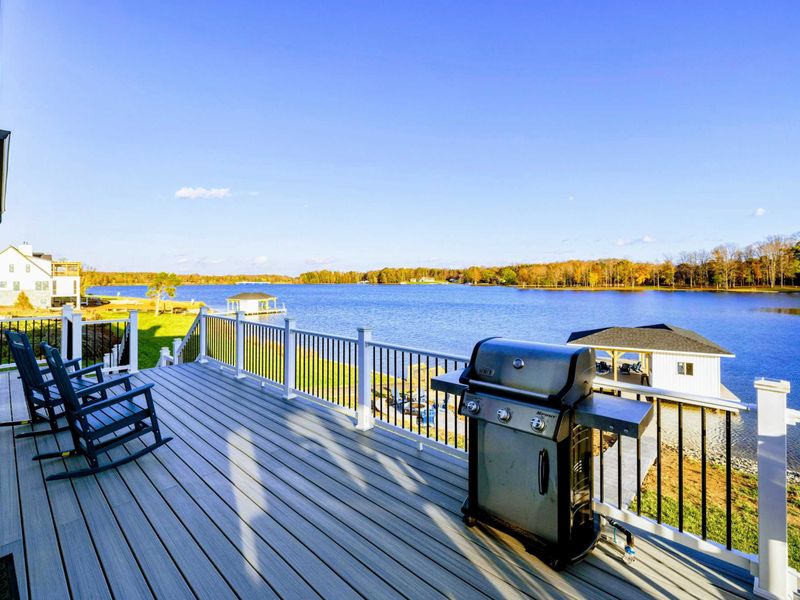 Spacious deck overlooking the lake, featuring rocking chairs and a grill for outdoor relaxation and dining.