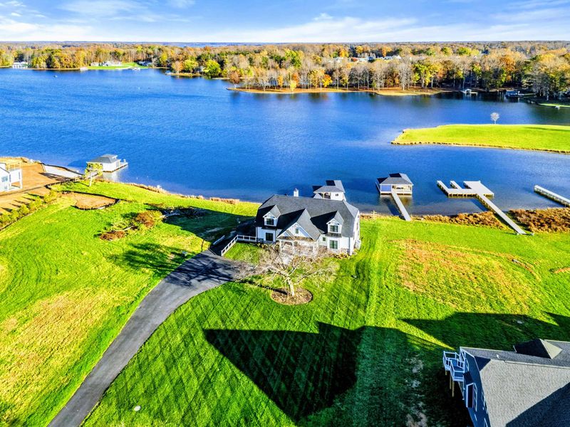 Beautiful lakeside property with a modern farmhouse-style home, a long paved driveway, and expansive green lawn overlooking the water.