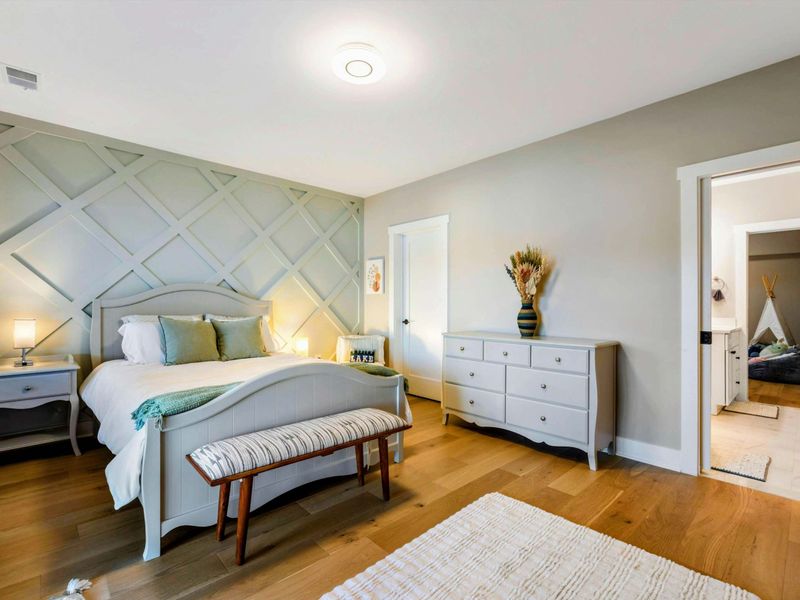 A cozy bedroom featuring a charming accent wall, elegant furnishings, access to the patio, serene views, and a Jack and Jill bathroom with a walk-in shower.