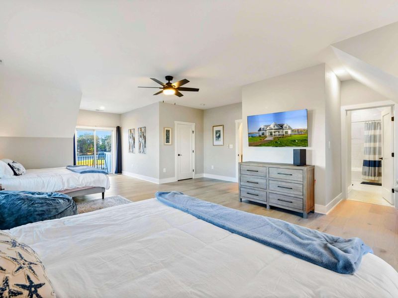A spacious and bright bedroom with multiple beds, a private balcony, an en-suite bathroom, and a cozy seating area, perfect for accommodating families or groups.