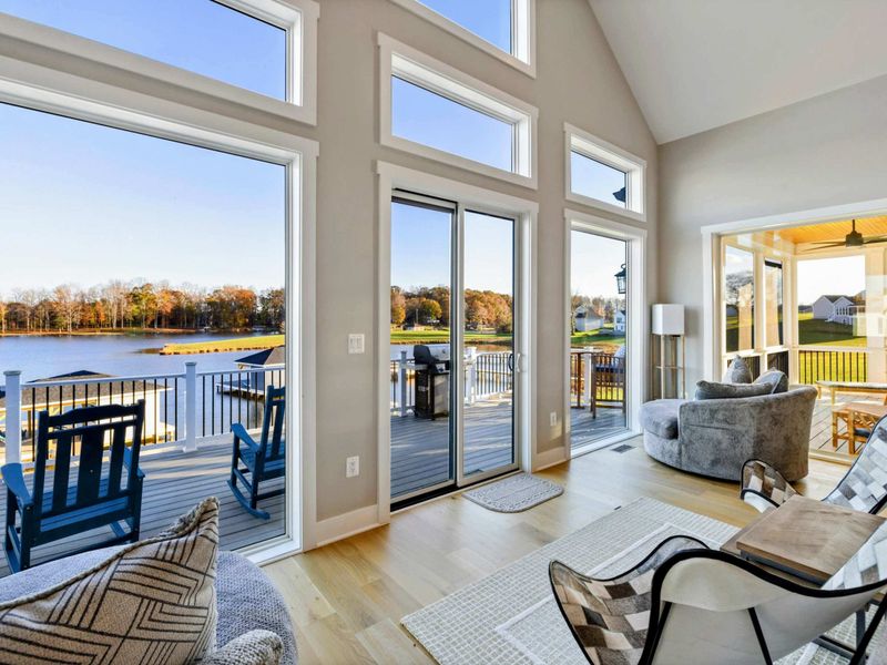 An airy living room with vaulted ceilings, stunning lake views through expansive windows, cozy seating, and direct access to a spacious outdoor deck.