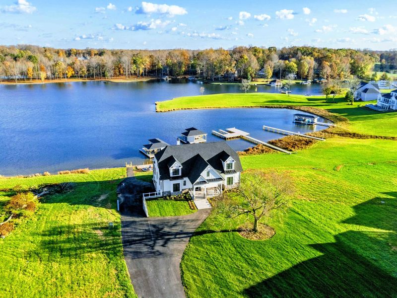 Beautiful lakeside property with a modern farmhouse-style home, a long paved driveway, and expansive green lawn overlooking the water.