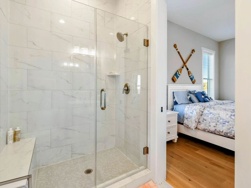 A shared Jack and Jill bathroom featuring a stylish vanity with a gold-framed mirror, soft lighting, and a walk-in shower for added convenience and comfort.