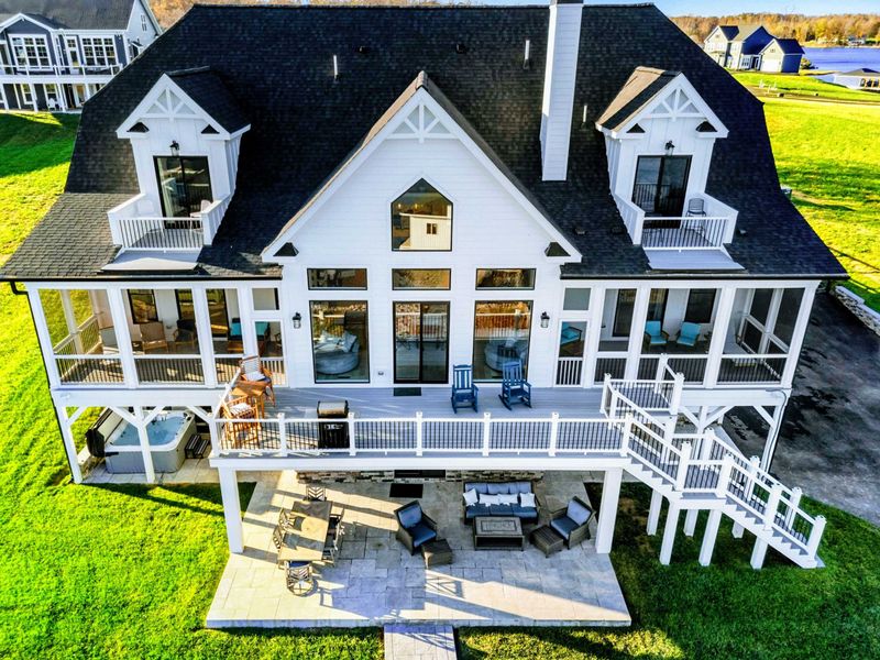 Expansive lakeside home with a modern farmhouse design, multiple balconies, screened porches, and a spacious outdoor patio for relaxation and entertainment.