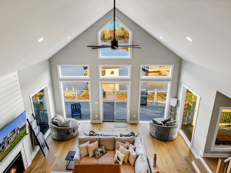 An airy living room with vaulted ceilings, stunning lake views through expansive windows, cozy seating, and direct access to a spacious outdoor deck.