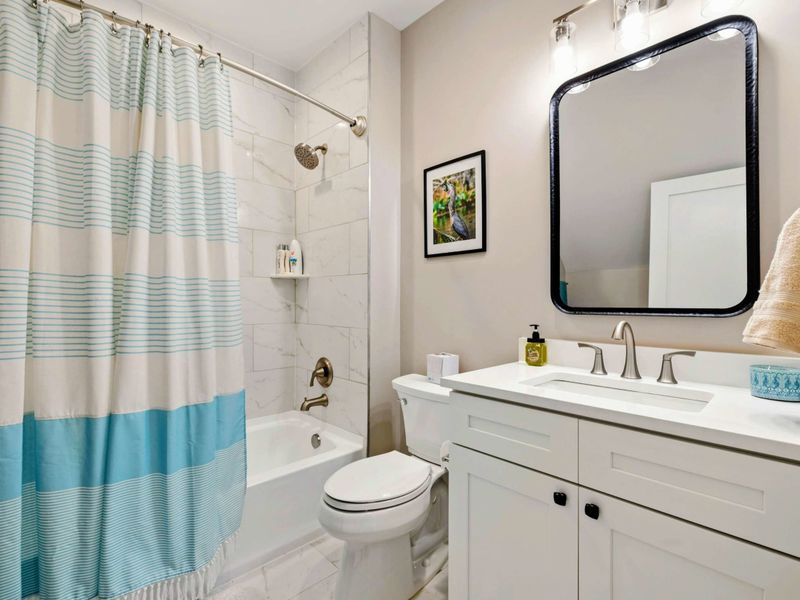 A clean and stylish bathroom featuring a tiled shower, a bright vanity with a large mirror, and cheerful accents for a welcoming feel.
