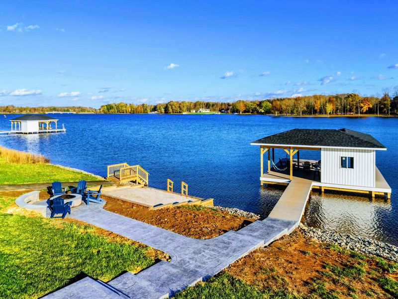 Lakeside area with a paved walkway leading to a private dock, a cozy fire pit with Adirondack chairs, and a swimming platform.