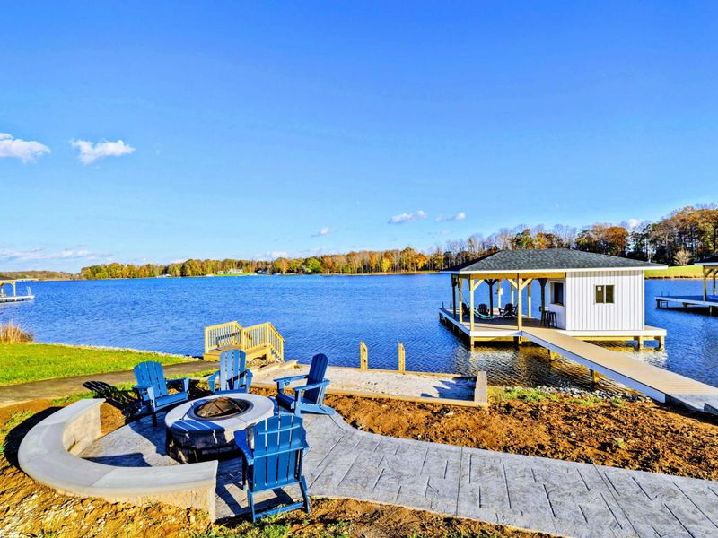 Lakeside area with a paved walkway leading to a private dock, a cozy fire pit with Adirondack chairs, and a swimming platform.