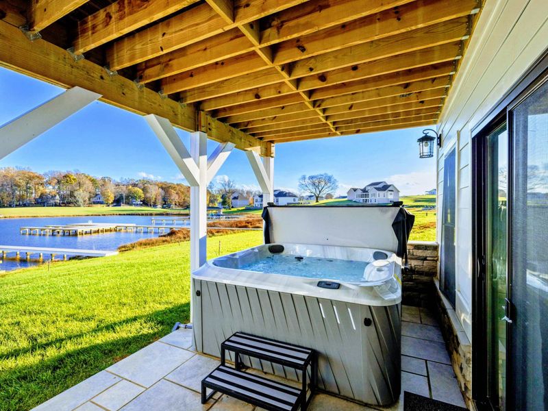 Covered patio featuring a relaxing hot tub with stunning views of the lake and nearby dock.
