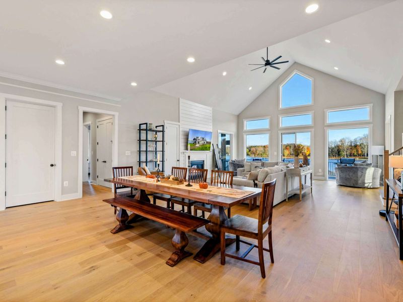 A bright and open living and dining space with vaulted ceilings, large windows offering scenic views, and comfortable seating, perfect for relaxing and entertaining.