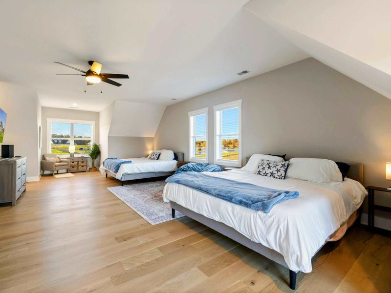 A spacious and bright bedroom with multiple beds, a private balcony, an en-suite bathroom, and a cozy seating area, perfect for accommodating families or groups.