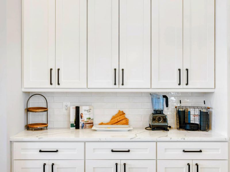 A sleek kitchen countertop with white cabinetry, modern appliances, and thoughtful touches like cookbooks and a blender, creating a functional and inviting space.