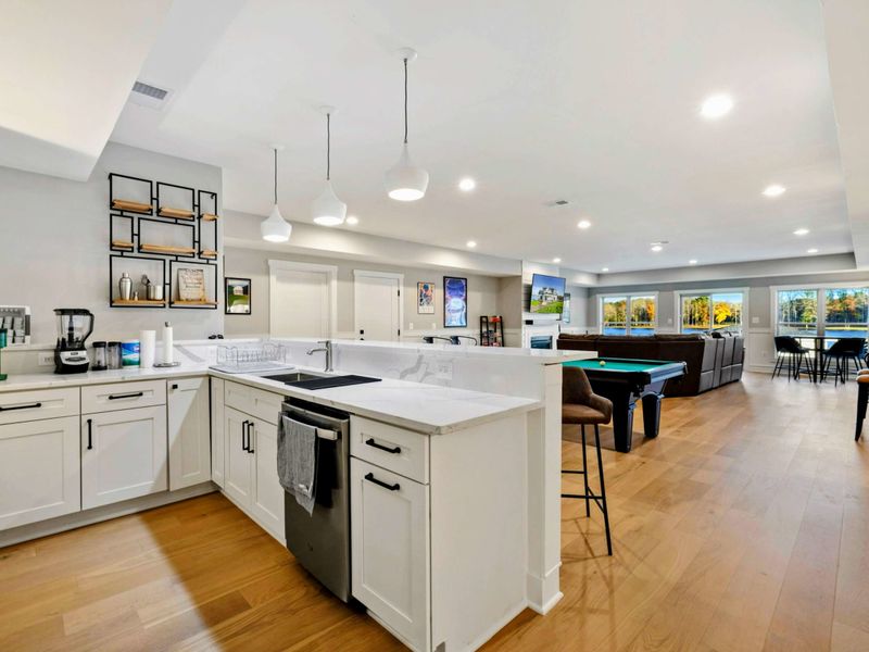 A modern open-concept kitchenette and entertainment area with bar seating, a pool table, and a cozy lounge space with large windows offering natural light and scenic views.