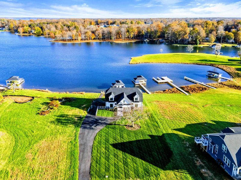 Beautiful lakeside property with a modern farmhouse-style home, a long paved driveway, and expansive green lawn overlooking the water.