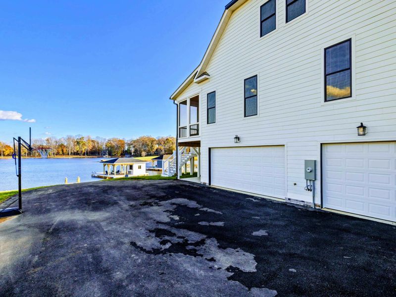 Large driveway with a three-car garage, basketball hoop, and stunning lakeside views.