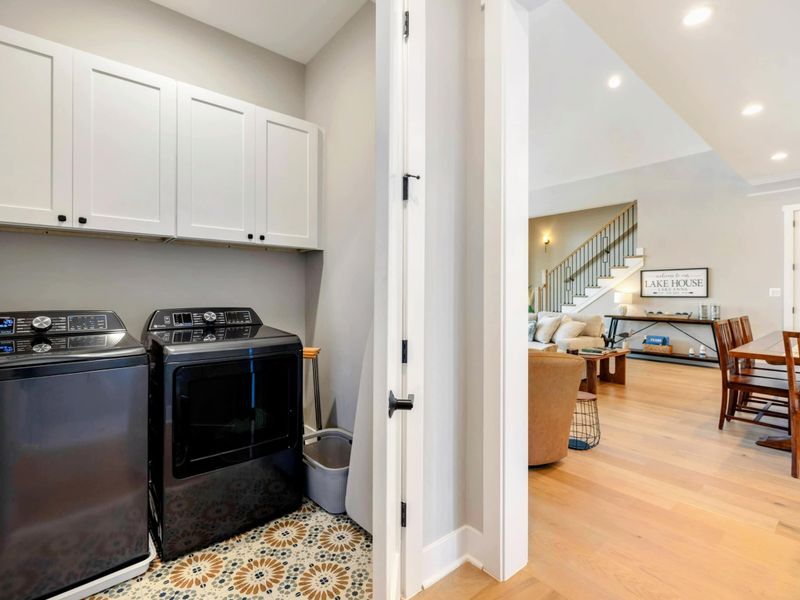 A convenient laundry room with modern appliances, stylish cabinetry, and patterned tile flooring, located just off the main living area.