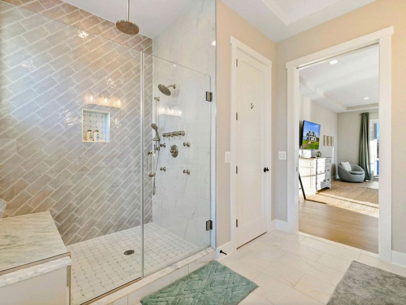 A spacious and elegant primary bathroom featuring a double vanity with gold-framed mirrors, a freestanding soaking tub, and a glass-enclosed walk-in shower with natural light.