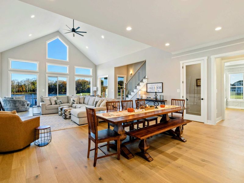 A bright and open living and dining space with vaulted ceilings, large windows offering scenic views, and comfortable seating, perfect for relaxing and entertaining.