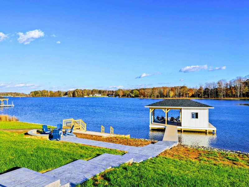 Lakeside area with a paved walkway leading to a private dock, a cozy fire pit with Adirondack chairs, and a swimming platform.