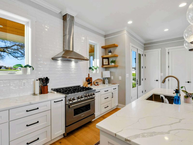 A modern and fully equipped kitchen with stainless steel appliances, elegant white cabinetry, a large center island, and stylish lighting for a perfect cooking and dining experience.