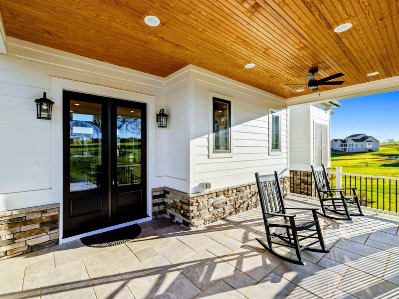 A welcoming front porch with rocking chairs, stone accents, a wood-paneled ceiling, and scenic views, perfect for relaxing and enjoying the outdoors.