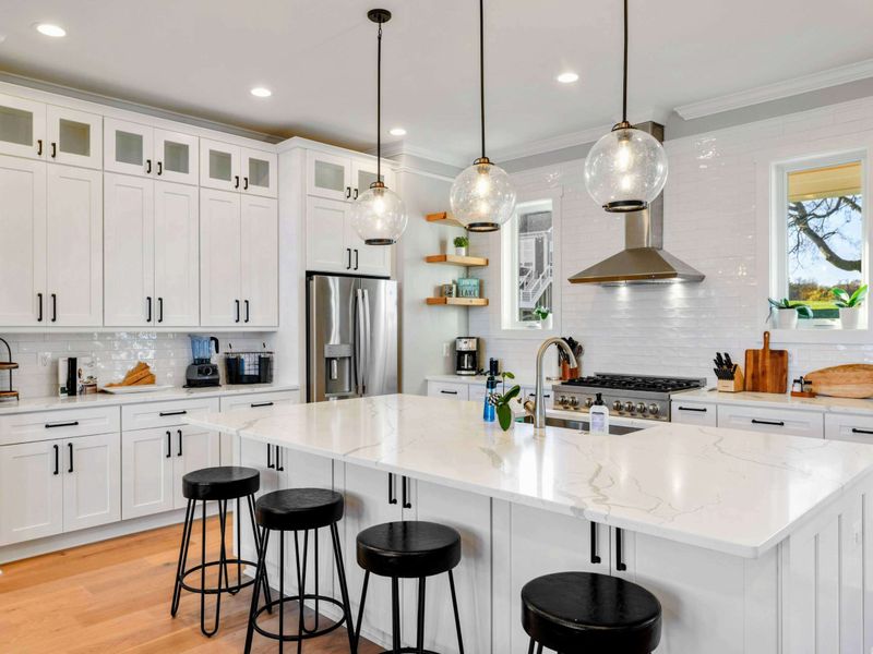 A modern and fully equipped kitchen with stainless steel appliances, elegant white cabinetry, a large center island, and stylish lighting for a perfect cooking and dining experience.
