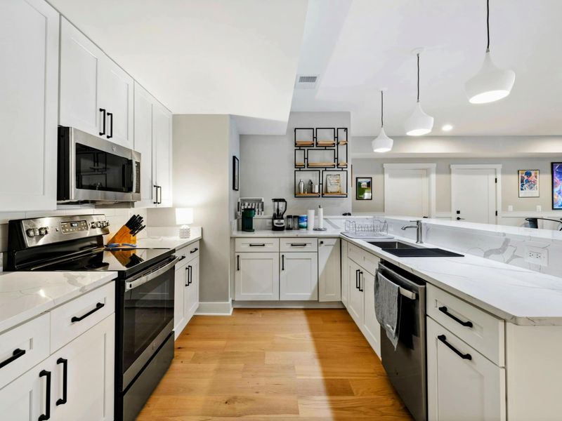 A stylish kitchenette with a sleek white design, modern appliances, pendant lighting, and comfortable bar seating for a casual dining experience.