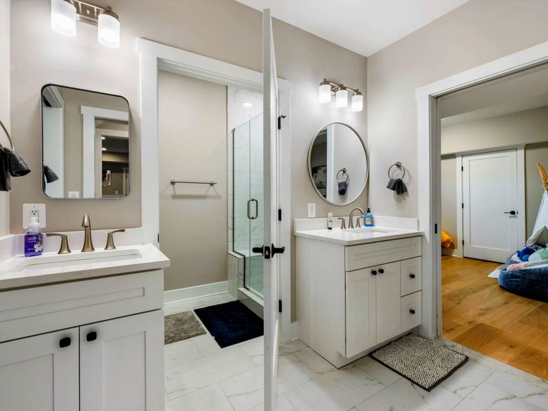 A spacious Jack and Jill bathroom featuring dual vanities, a modern walk-in shower, and convenient access to connecting bedrooms.