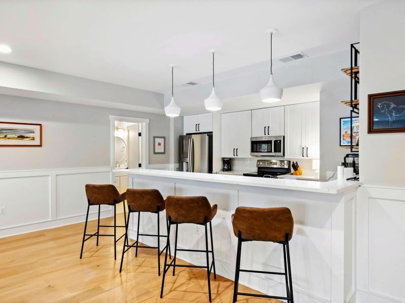 A stylish kitchenette with a sleek white design, modern appliances, pendant lighting, and comfortable bar seating for a casual dining experience.
