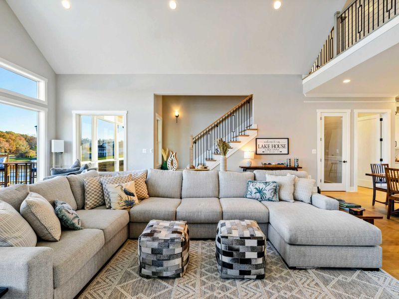 Bright and airy living room with a large sectional sofa, vaulted ceilings, and stunning lake views through expansive windows.