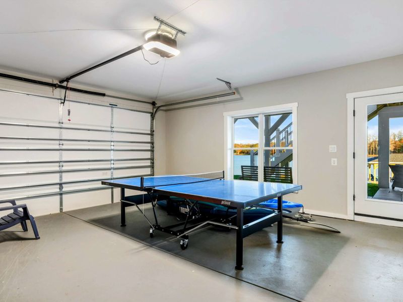A versatile game room with a ping pong table, garage access, and sliding doors leading to an outdoor space with scenic views.