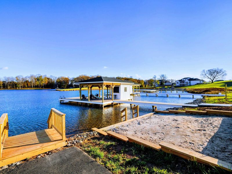 Lakeside area featuring a sandy volleyball court, a dock with a covered boat slip, and peaceful waterfront views.