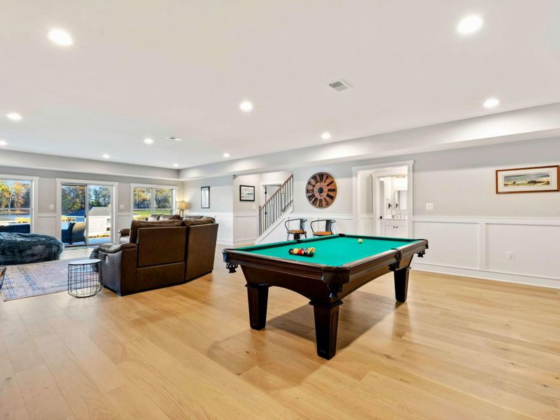 A bright and inviting recreation area with a pool table, comfortable seating, a bar area, and large windows showcasing scenic views.