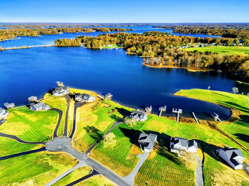 Aerial view of a tranquil lakeside community featuring spacious homes, green lawns, and private docks with stunning water views.