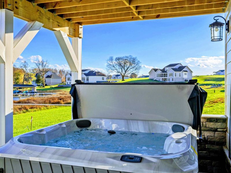 Covered patio featuring a relaxing hot tub with stunning views of the lake and nearby dock.