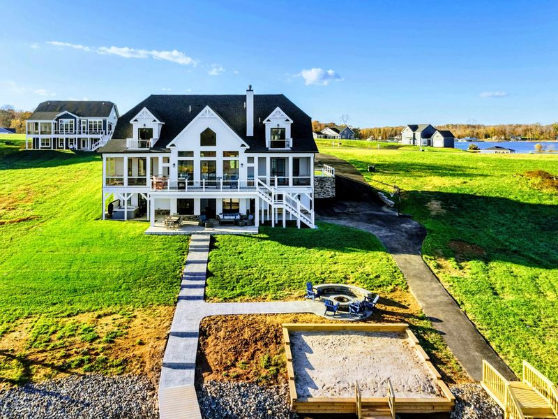Lakeside home featuring a spacious lawn, multiple decks, a fire pit, and a private sandy area with direct water access for outdoor enjoyment.