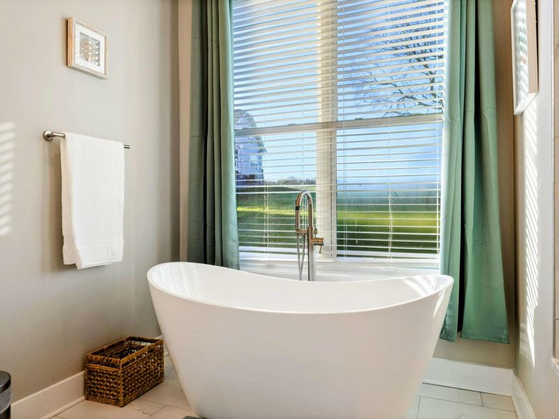A spacious and elegant primary bathroom featuring a double vanity with gold-framed mirrors, a freestanding soaking tub, and a glass-enclosed walk-in shower with natural light.