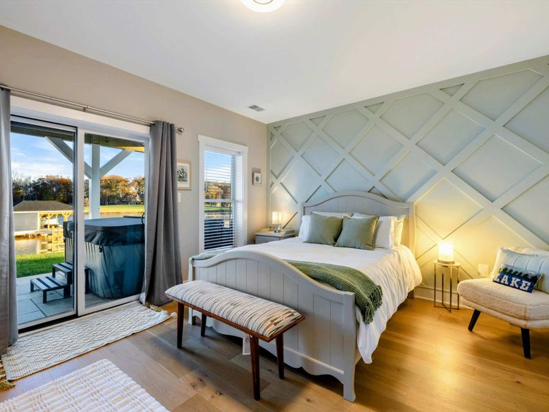 A cozy bedroom featuring a charming accent wall, elegant furnishings, access to the patio, serene views, and a Jack and Jill bathroom with a walk-in shower.